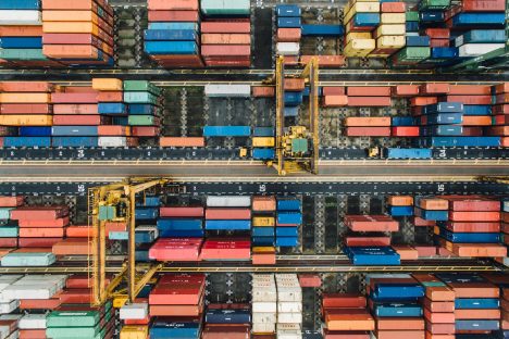 Vue aérienne d'un port de conteneurs avec des grues et des rangées de conteneurs colorés, symbolisant la gestion des transpor